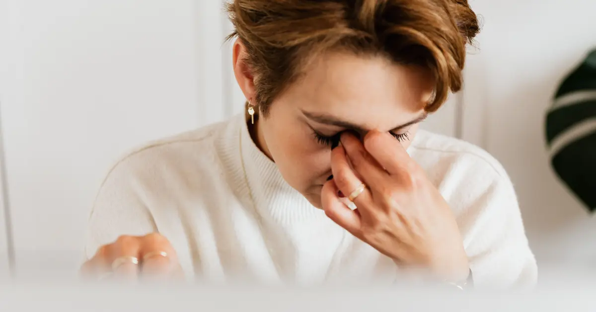 Woman rubbing itchy, watery eyes from a cat allergy with her cat resting close by