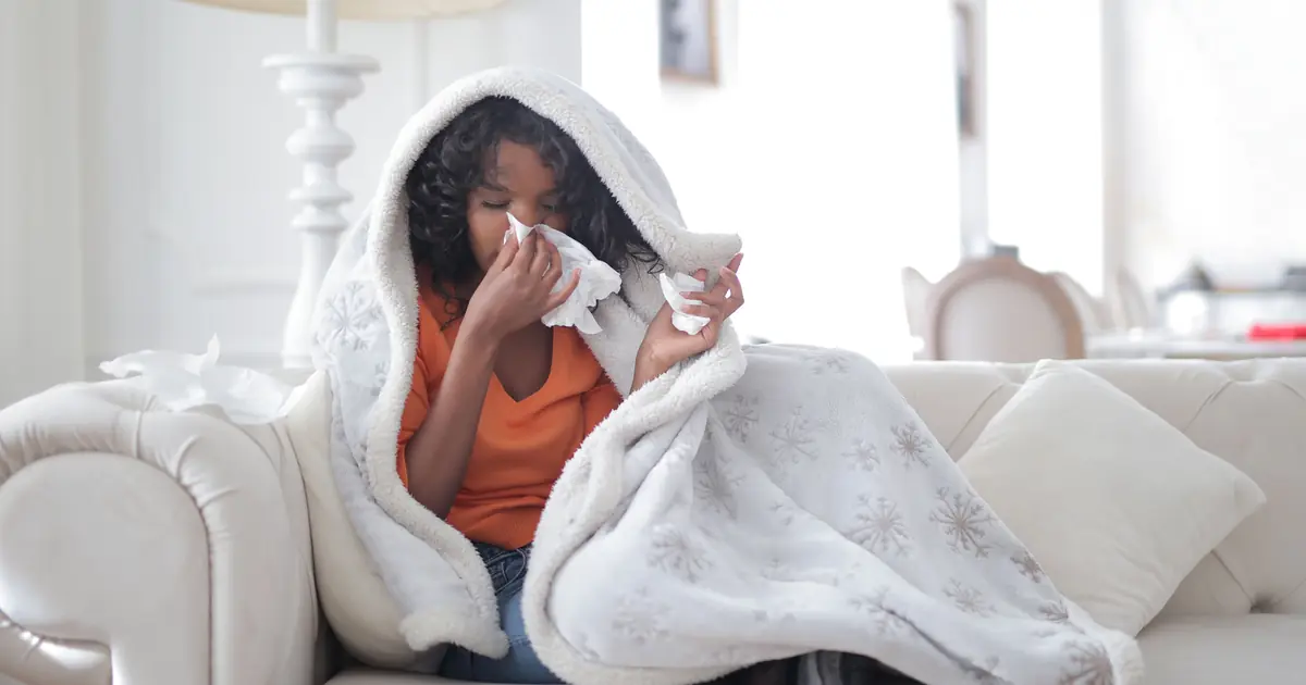 A person sneezing into a tissue while sitting near their cat, showing cat allergy symptoms